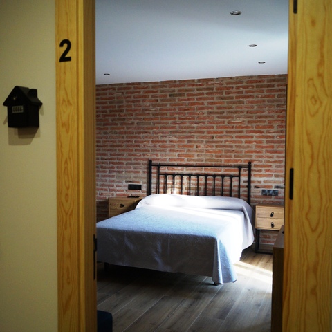 Habitación número 2 de la Casa Rural La Josefa, en Fermoselle, equipada con cama de matrimonio, cabecero de hierro y pared de ladrillo, perfecta para estancias en las Arribes del Duero.