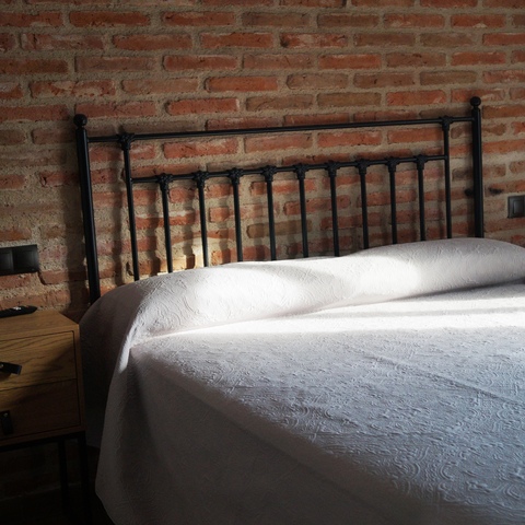 Detalle del cabecero de hierro forjado junto a la pared de ladrillo en la habitación número 2 de la Casa Rural La Josefa en Fermoselle.